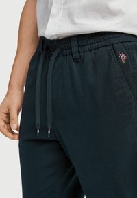 Tmavě modré bavlněné šortky jogger s elastickým pasem, nastavitelnými šňůrkami a malým vyšitým logem na levém stehně.