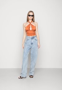 Top de cetim laranja às tiras com um detalhe em forma de buraco e calças de ganga de cintura alta e pernas largas em azul claro. Óculos de sol pretos e sandálias rasas completam o visual.