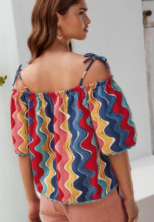 Krāsains, daudzkrāsains topiņš ar viļņotu rakstu sarkanā, zilā, dzeltenā un rozā krāsā. Elastīga apkakle ar saistiem siksnām un viļņotu apakšu.