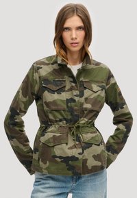 Camouflage jack met een trekkoord in de taille, twee borstzakken en lange mouwen, gemaakt van een duurzaam materiaal in groen- en bruintinten.