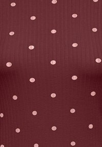 Bordeauxrode top met geribbelde textuur, voorzien van gelijkmatig verdeelde lichtroze polkadots. Het ontwerp benadrukt een aansluitende pasvorm en een modern patroon.