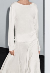 Kermanvalkoinen, pitkähihainen yläosa pehmeästä kankaasta, yhdistetty vastaavaan, soljuvaan hameeseen, jossa on hieman teksturoitu pinta ja rento istuvuus.