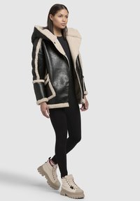 Sort læderjakke med beige kunstpelsdetaljer, hætte og lynlås. Matchet med sorte leggings og beige chunky sneakers.