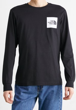 Chemise noire à manches longues en coton avec un col rond. Comprend une poche poitrine avec un logo graphique blanc. Coupe décontractée et confortable.