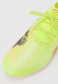 Ljusgul fotbollssko med texturerad yta, med rosa accenter och strömlinjeformat design; inkluderar perforerade områden för andningsförmåga.