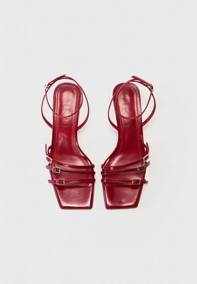 Czerwone lakierowane szpilki slingback z kwadratowymi noskami, z trzema paskami i metalowymi klamrami. Gładzona, błyszcząca powierzchnia.