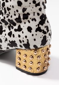 Skórzane botki za kostkę w czarno-białą cętkowaną wzór, z złotą popękaną obcasem ozdobionym metalowymi ćwiekami.