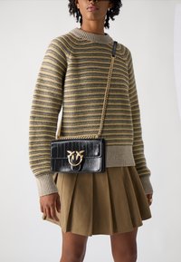 Melnas patentētas ādas crossbody soma ar zeltīta metāla detaļām, ar taisnstūra formu un ķēdes siksnu. Apvienota ar svītrotu džemperi un pleitotu svārku.