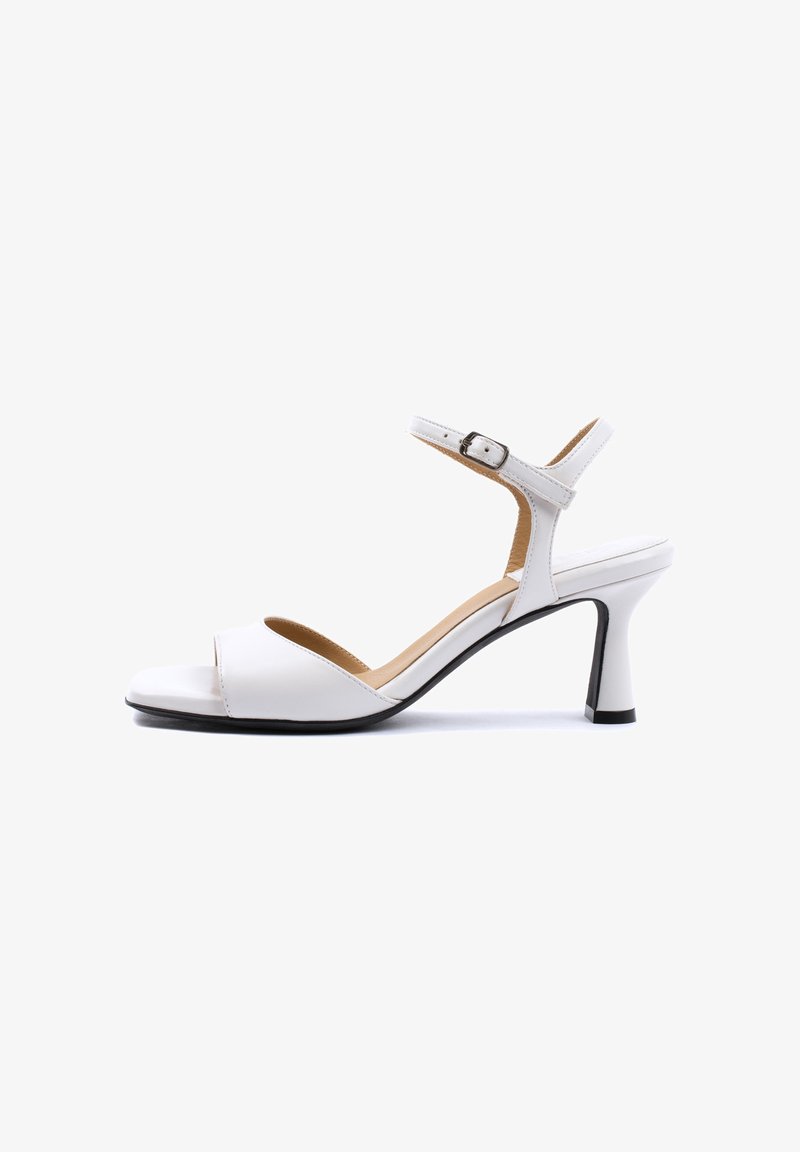 Sandale blanche à talon haut ouverte à l’avant, avec bride à la cheville et boucle, talon incurvé et semelle intérieure rembourrée, vue de côté sur fond blanc.