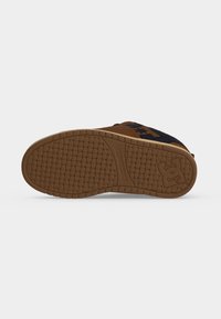 Semelle d'une chaussure de sport marron et noire avec un motif de bande de roulement texturé et un logo stylisé près du talon.