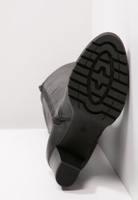Botín negro con parte superior de cuero texturizado, puntera cuadrada y tacón bajo. La suela de goma cuenta con un patrón de tracción. Detalle de cremallera en el lateral.
