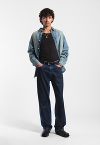 Džínová košile v světle modré, přes černé tílko; tmavé džínové kalhoty; černý opasek; lesklé černé boty. Čistý, casual styl.