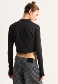Black cropped long-sleeve top, fitted design, smooth texture. Paired with gray checkered pants featuring rear pockets and a black label.