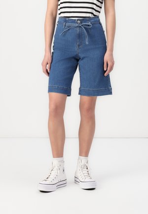 Denim shorts med høy midje, lyseblå farge, oppbrettede kanter og snor. Kombinert med hvite høye sneakers.