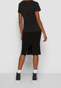 Černé bavlněné tričko s krátkým rukávem, spárované s černou žebrovanou sukní s rozparkem na zadní straně. Model má na sobě černé kotníkové boty s bílou podrážkou.