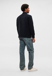 Navy sako od somota s ovratnikom, vidljivim šavovima i detaljima s gumbima, uparen s svijetloplavim trapericama opuštenog kroja i bijelim tenisicama.