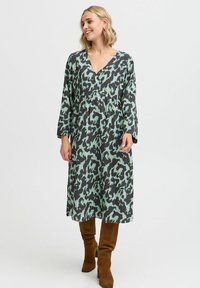 Rochie cu mâneci lungi, în nuanțe de negru și verde mentă cu un model abstract. Design cu decolteu în V, croi lejer, lungime medie, asortată cu cizme marron până la genunchi.