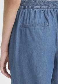 Mėlynos chambray kelnės su elastingu juosmeniu, turinčios vieną užpakalinę kišenę ir lygaus audinio tekstūrą.