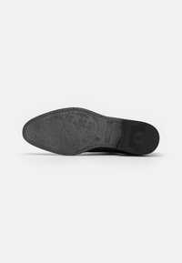 Suola in gomma nera con texture a motivi e logo. Presenta una forma arrotondata con un leggero tacco e una parte anteriore piatta per maggiore stabilità.