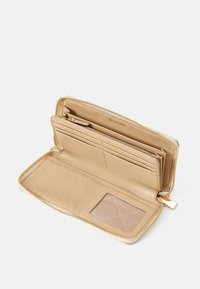 Beige leather zip-around wallet open to show multiple card slots, a clear ID window, a zippered coin compartment, and "Michael Kors" logo inside.