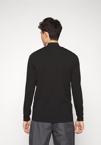 Czarna koszula z długim rękawem i wysokim kołnierzem, z białymi paskami na rękawach. Wykonana z gładkiego, lekkiego materiału.