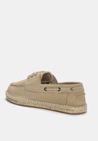 Beige espadrille velúrbőr felsőrésszel, kerek orral, az oldalán fűzéssel és juta kötegből készült talppal. Lapos profil és nyitott hátsó dizájn a könnyű felvétel érdekében.