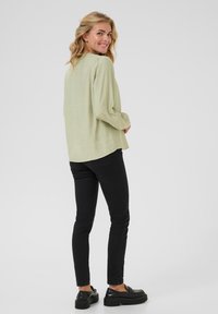 Light green long-sleeve shirt with a relaxed fit, textured fabric, and rounded hem, paired with black slim-fit jeans and black shoes.