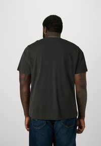 Black short-sleeve T-shirt made of cotton, featuring a round neckline and a relaxed fit. Worn with blue denim jeans.