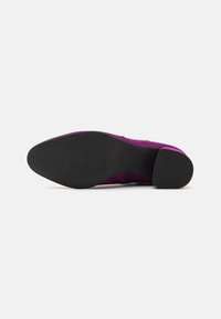 Purple suede shoe with a black rubber sole, featuring a smooth texture and a low block heel.  Curved lines along the side of the shoe.