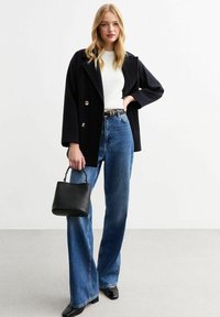 Svart dubbelknäppt kappa, grå tröja, hög midja blå jeans, svart handväska med kedja och svarta spetsiga klackar.