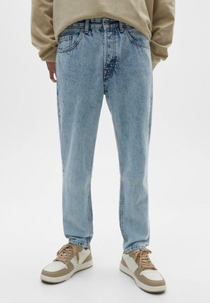 Light blue relaxed-fit jeans worn with beige and white sneakers and a beige long-sleeve top, shown from waist to feet.