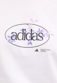T-shirt bianco con un design floreale con accenti viola e il logo "adidas". Il testo include "RADIATE YOUR ESSENCE" e un piccolo logo.