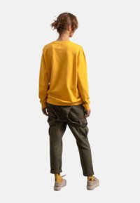 Sweatshirt giallo in cotone con colletto a girocollo e polsini a coste, abbinato a pantaloni cargo verdi con molteplici tasche e cinghie regolabili.