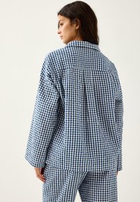 Niebiesko-biała piżama w kratkę vichy, składająca się z koszuli z kołnierzykiem, długimi rękawami i luźnym krojem, z guzikowym zapięciem z tyłu i plisowanymi detalami.