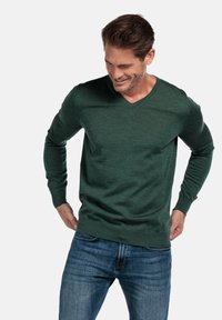 Groene V-hals trui van zacht materiaal, met lange mouwen en een relaxed fit. Gecombineerd met casual blauwe jeans.