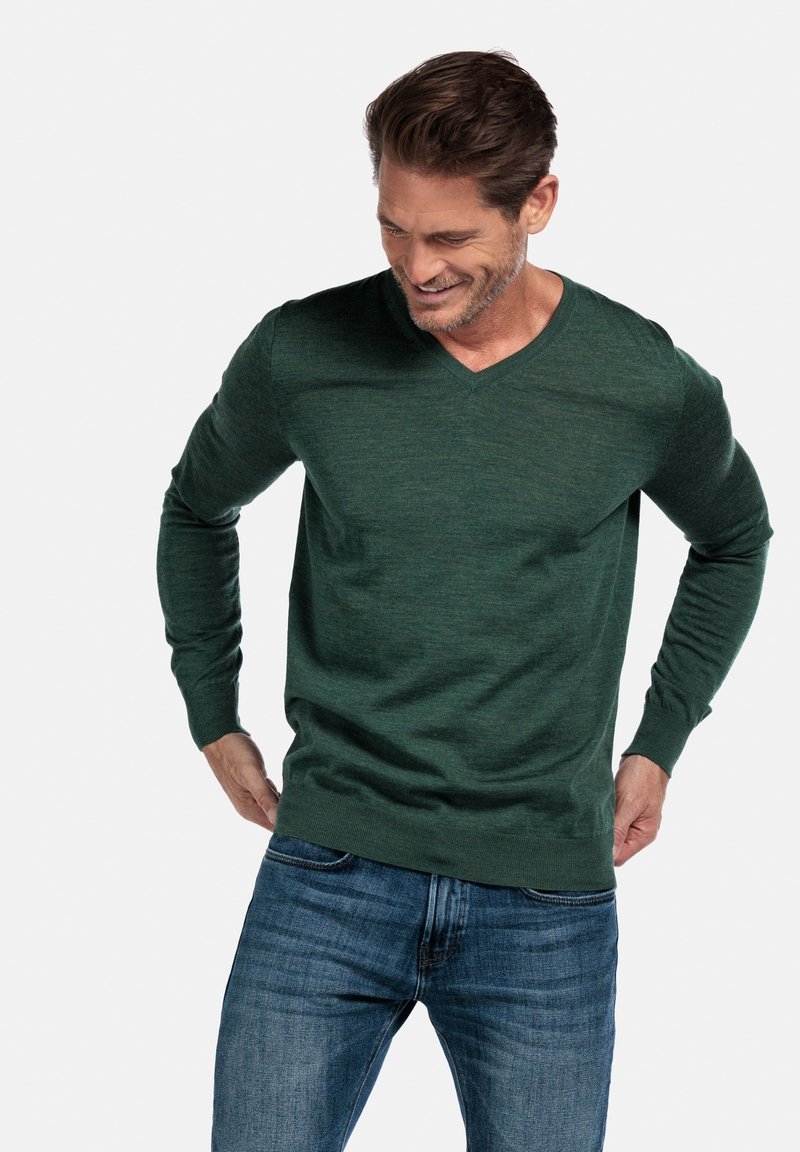 Groene V-hals trui van zacht materiaal, met lange mouwen en een relaxed fit. Gecombineerd met casual blauwe jeans.