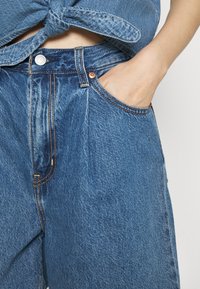 Jeans aus Denim mit hoher Taille, in hellblau, mit kupferfarbener Hardware und orangen Nähten. Verfügt über Fronttaschen und ein lässiges Design.