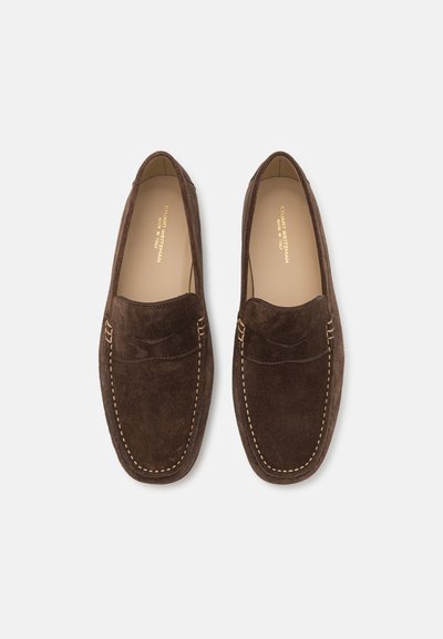 Mocassins en daim marron avec détails de couture et design mocassin. Possède une texture lisse et un bout arrondi. Logo doré sur la semelle intérieure.