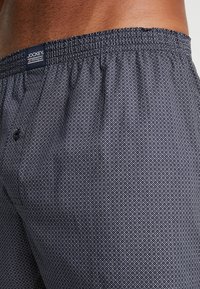Navy geprinte boxers met een diamantpatroon, elastische tailleband en een enkele knoopsluiting. Etiket leest "Jockey USA Originals."