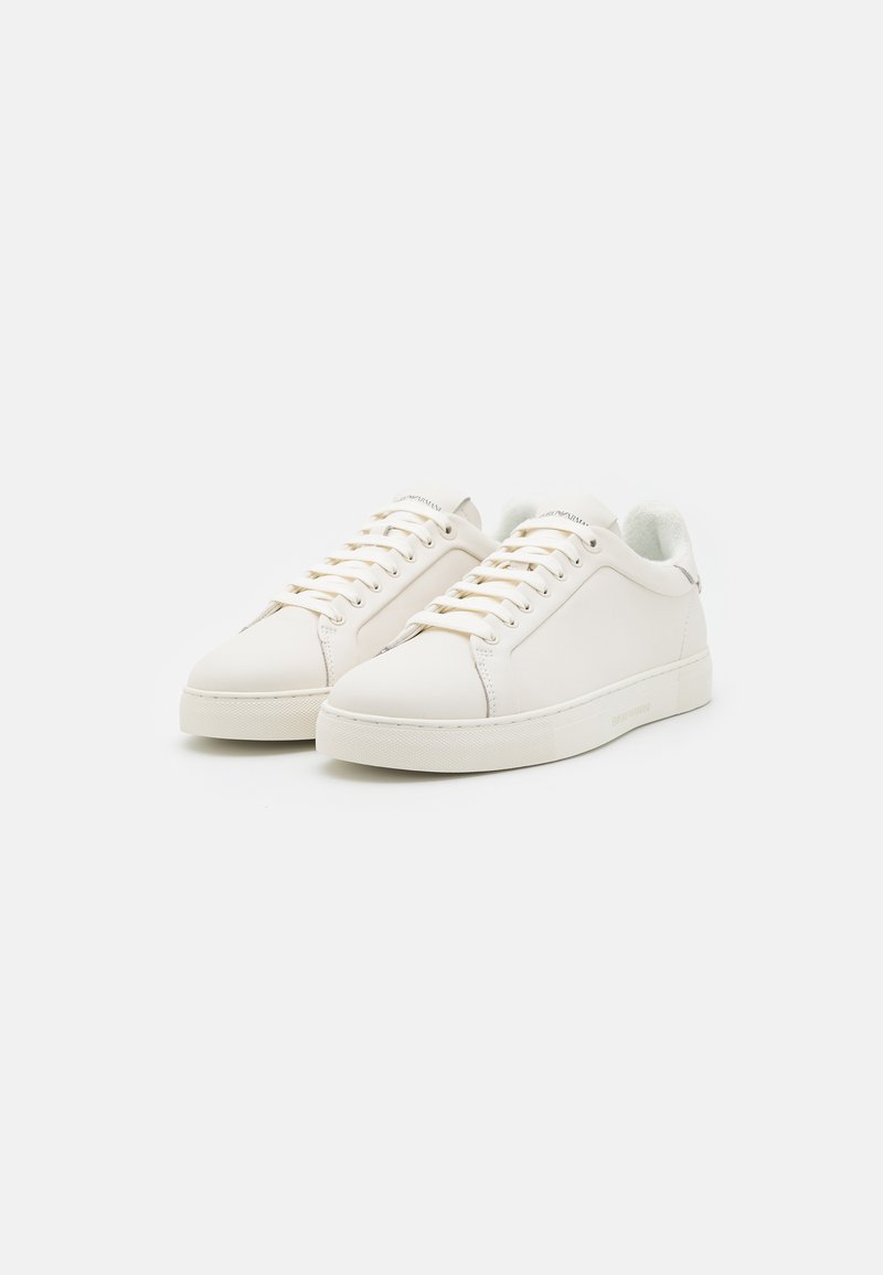 Baskets en cuir blanc avec une texture lisse, bout rond et semelle plate. Présentent des coutures minimes et un système de laçage avec un logo discret.