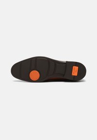 Musta kumipohja, jossa on teksturoitu pinta, ja jossa on pyöreä oranssi yksityiskohta sekä urat pidon parantamiseksi. Vahvistettu kantapää.