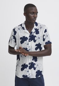 Camicetta a maniche corte con base bianca e stampa floreale blu navy, dotata di colletto a camicia e vestibilità rilassata. Tessuto morbido, design casual.