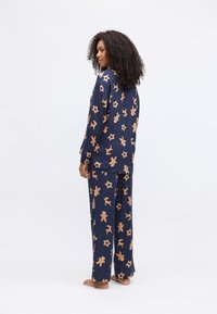 Marineblauw pyjamapakket met afbeeldingen van peperkoekjes en sterrenpatronen, gemaakt van zachte stof met een relaxte pasvorm. Inclusief lange mouwen en wijde broek.