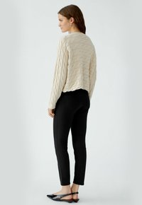 Gebreid sweater in crème met een getextureerd golfpatroon, gecombineerd met zwarte skinny jeans en platte slingback schoenen, gezien vanuit de achterkant.