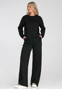 Czarna bluza z kieszenią, zestawiona z czarnymi szerokimi spodniami. Gładka tekstura, casualowy fason i minimalistyczny styl. Białe sneakersy.