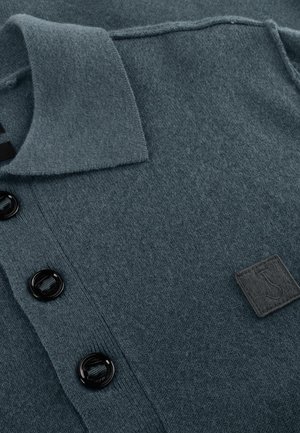 Donker teal gebreide polo shirt gemaakt van zachte stof, met een kraag, drie zwarte knopen en een gestructureerd ontwerp met een klein logo-embleem.