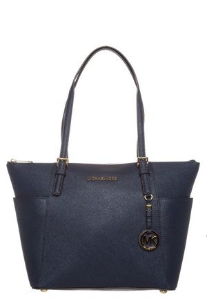 Granatowa torba typu tote Michael Kors z podwójnymi rączkami, złotą plakietką z logo i okrągłą zawieszką MK wiszącą na jednej rączce.