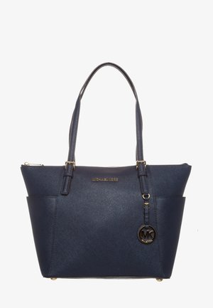 Granatowa torba typu tote Michael Kors z podwójnymi rączkami, złotą plakietką z logo i okrągłą zawieszką MK wiszącą na jednej rączce.