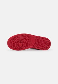 Semelle extérieure en caoutchouc rouge d'une chaussure Nike avec des motifs de bande de roulement circulaires et en grille, incluant le logo Nike près du centre.