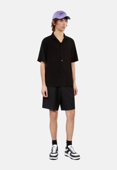 Zwarte T-shirt met korte mouwen, zwarte shorts en zwart-witte sneakers. Lichtpaarse pet met tekstdetail. Casual fit, minimalistisch ontwerp.